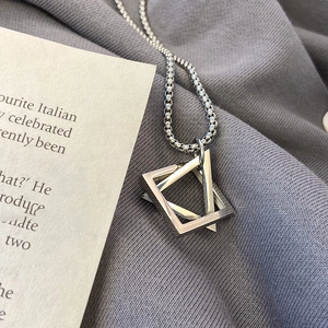 Close-up of interlocking silver geometric triangle and square pendant on a grey fabric background