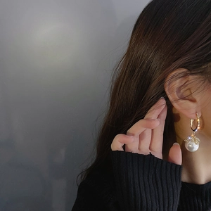 Detail of gold zircon hoop earrings with a large white pearl drop on a female model