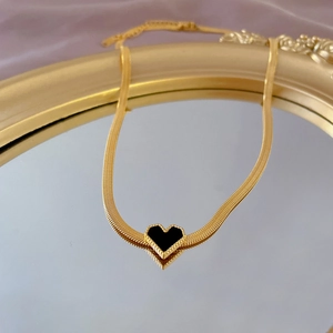 Detail of gold snake chain with black heart pendant on a gold mirror display