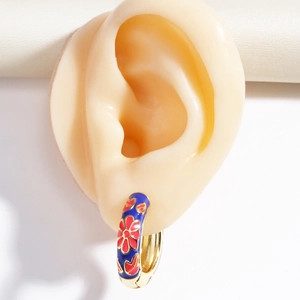 Blue enamel huggie hoop earring with pink flower pattern on a realistic ear model