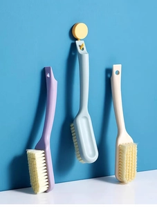 Three macaron-colored cleaning brushes with long handles and soft bristles on a blue wall