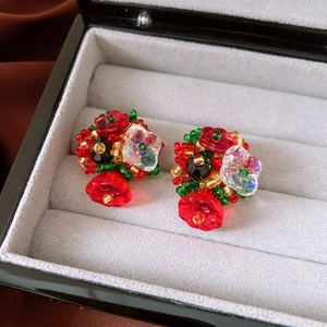 Macro shot of handmade floral beaded earrings with red and green glass beads in a gift box