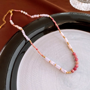 Detail of beaded necklace with pink stones and gold chain in a ceramic tray