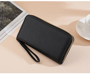 Detailed view of black textured leather long wallet with wrist strap on a stylish desk