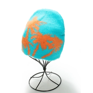 Close-up of a light blue knit beanie with orange palm tree pattern on a metal stand