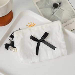 Close-up of white lace makeup bag featuring a black bow and pearl keychain detail