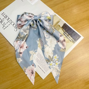 Close-up of a light blue satin bow hair clip with floral print and long ribbon tails
