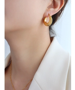 Gros plan d'une boucle d'oreille créole dorée texturée portée par un mannequin chic