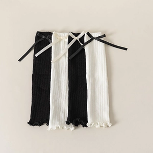 Detail of knitted leg warmers with ribbon bows and ruffled edges in black and white