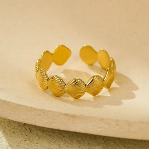 Bague ouverte coquillage plaquée or 18 carats sur un socle d'exposition beige