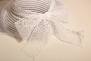 Vue détaillée d'un élégant chapeau de paille blanc avec un nœud en dentelle et perles.