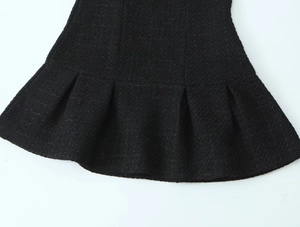 Macro detail showing the black tweed fabric texture and pleated hem of the French style dress