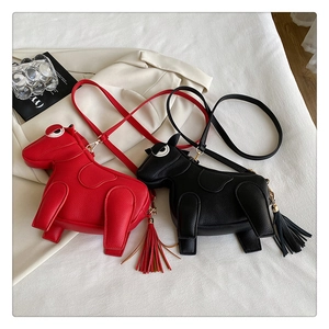 Top view of red and black horse-shaped crossbody bags with tassels on white fabric