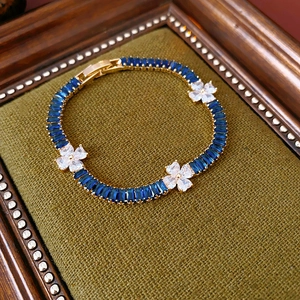 Detailed close-up of a gold bracelet with blue crystals on dark green velvet