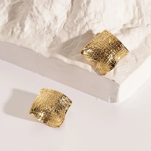 Detailed close-up of gold square stud earrings with irregular hammered texture on stone