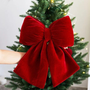 Velvet red Christmas bow ornament decorating a lit Xmas tree for festive atmosphere