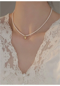 Detail of freshwater pearl choker featuring a polished 14K gold heart pendant on a model