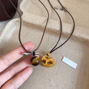 Detailed shot of tiger eye bead and golden rocking horse pendant necklaces with brown cords