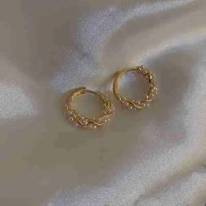 Elegant gold twisted hoop earrings with small pearls on white silk background