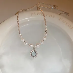 Silver teardrop necklace with blue gemstone and white pearls on stone tray