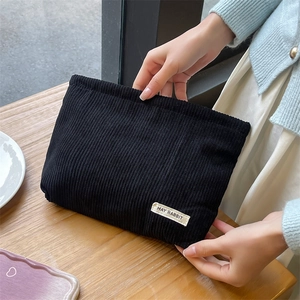 Close-up of a black corduroy makeup bag held by hands on a wooden cafe table