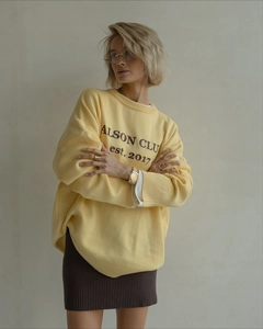 Detail of yellow knit crewneck sweater with ALSON CLUB print and dark brown mini skirt