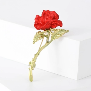 Elegant vintage rose brooch with red petals and golden stem on white pedestal