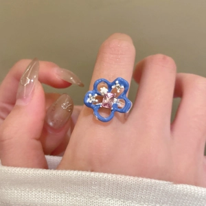 Detailed shot of an open ring featuring blue floral enamel and a pink rectangular crystal
