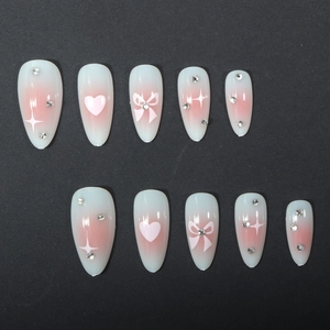 Almond press-on nails with pink ombre, heart designs and rhinestones on black background