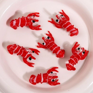 Top view of six handcrafted red and white glass crayfish pendants in a white ceramic dish