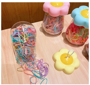 Colorful hair bands set in transparent flower-shaped jars on a light wood surface