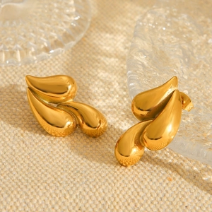 Boucles d'oreilles feuilles en acier inoxydable doré 18 carats sur lin beige