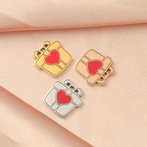 Drei herzförmige Geschenkbox-Anhänger in Gold, Roségold und Silber auf rosa Seide