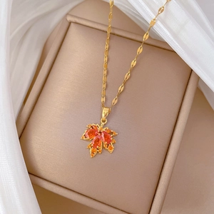 Detail of gold maple leaf necklace with orange gemstone in a beige jewelry gift box
