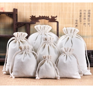 Various sizes of cream canvas drawstring jewelry pouches stacked on a wooden stand