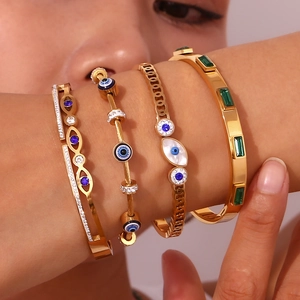 Detail of four gold-plated stainless steel evil eye bracelets layered on a wrist