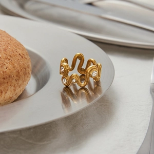 Détail d'une bague vague en or titane avec zircons sur un plateau en métal brossé