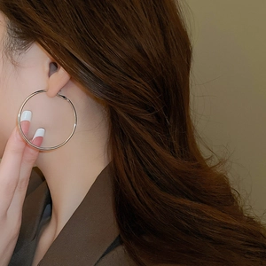 Close-up of model wearing large polished silver hoop earrings with minimalist design