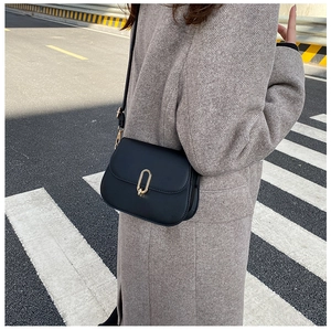 Detail of a matte black saddle bag with a gold oval clasp worn on a grey wool coat
