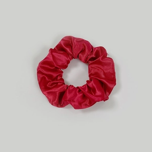 Close-up of bright red satin scrunchie showing soft pleated texture and silky sheen