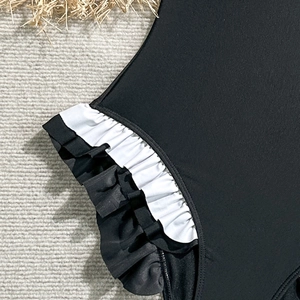 Detailed view of the black one-piece swimsuit featuring elegant white ruffled hem detail