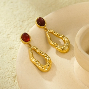 Close-up of vintage gold earrings with deep red oval stones on beige ceramic texture