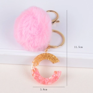 Pink pompom and glitter resin letter C keychain with gold hardware on white steps