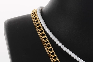 Detail of layered gold metal chain and white faux pearl necklace on black display