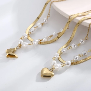 Detail of double-layered gold snake chain with heart, butterfly and pearls
