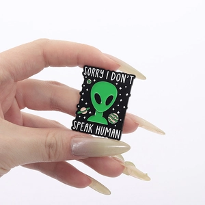 Close-up of green alien enamel pin with Sorry I Don't Speak Human slogan on hand