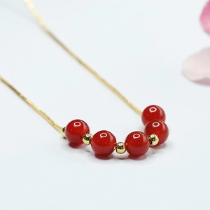 Détail de perles d'agate rouge et d'entretoises dorées sur un collier minimaliste