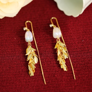 Detail shot of long tulip pearl tassel earrings with gold leaves on red texture