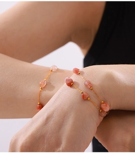 Detail of a gold chain bracelet featuring translucent red agate beads on a female wrist