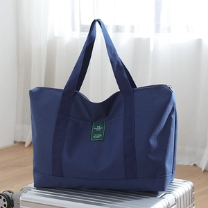 Large dark blue canvas travel tote bag placed on a silver suitcase in a bright room